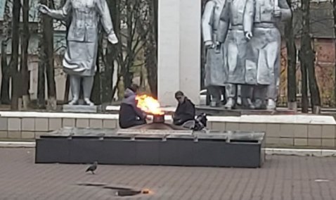 Двое мужчин в Ожерелье грелись и выпивали у Вечного огня, сидя на памятнике